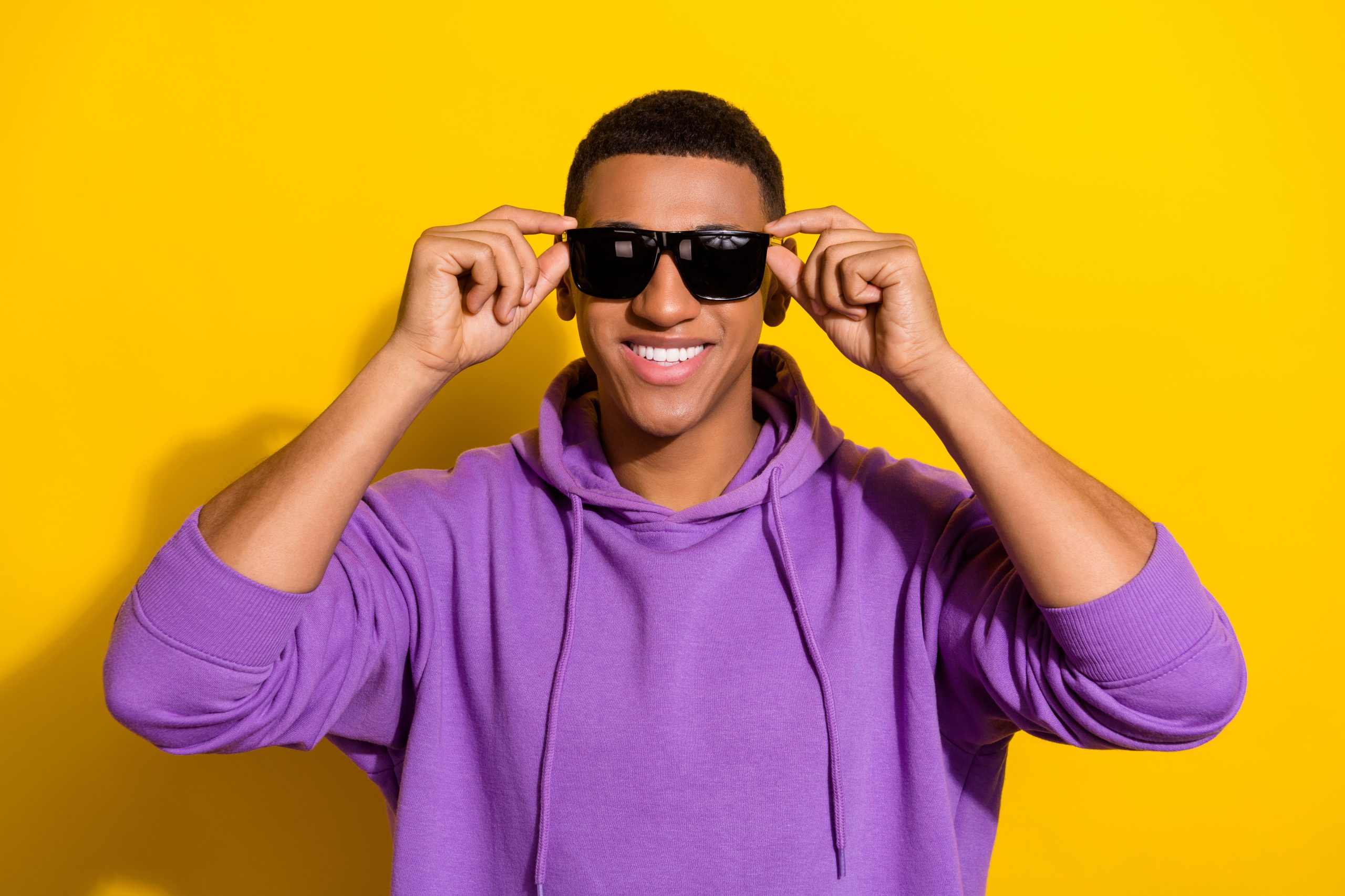 Portrait of attractive cheerful guy touching specs modern street style isolated over bright yellow color background